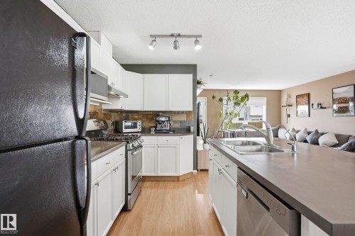 Kitchen featuring light wood-finish flooring, white cabinetry, stainless steel appliances, and a tiled backsplash - 14017 156 Avenue, Edmonton, AB - Indoor Photo Showing Kitchen With Double Sink