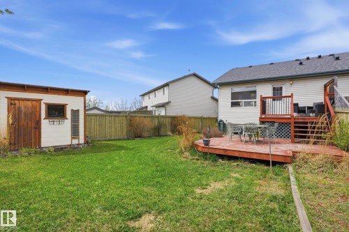 Expansive backyard featuring a wood deck with stairs, a white shed with a natural wood door, a wooden fence, and a green lawn - 14017 156 Avenue, Edmonton, AB - Outdoor With Deck Patio Veranda