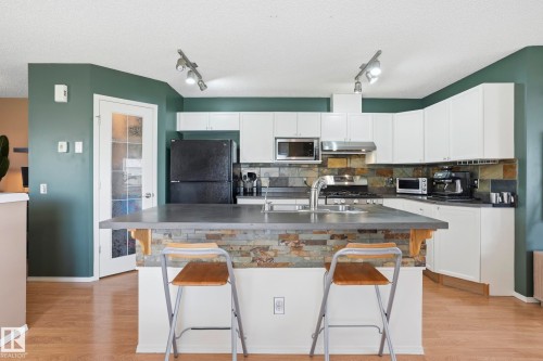 Contemporary kitchen featuring white cabinetry, a stone backsplash, stainless steel appliances, and a central island with integrated sink - 14017 156 Avenue, Edmonton, AB - Indoor Photo Showing Kitchen With Double Sink