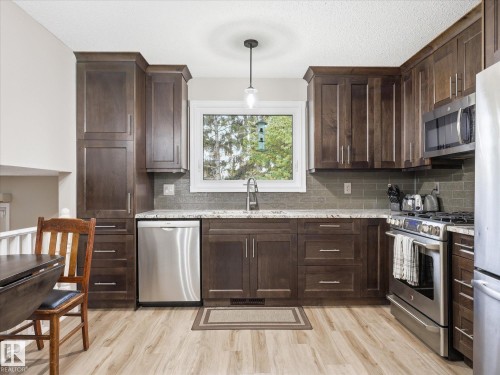 Modern kitchen featuring wood-finish flooring, dark wood cabinetry with stainless steel hardware, and a light-toned countertop - 18627 62A Avenue, Edmonton, AB - Indoor Photo Showing Kitchen With Upgraded Kitchen