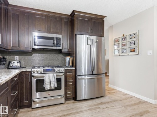 Kitchen featuring dark wood-finish cabinetry, stainless steel appliances, granite countertops, a textured backsplash, and wood-finish flooring - 18627 62A Avenue, Edmonton, AB - Indoor Photo Showing Kitchen With Upgraded Kitchen
