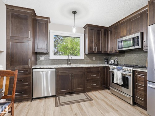 Kitchen featuring rich wood cabinetry, light-toned wood-finish flooring, and a subway tile backsplash - 18627 62A Avenue, Edmonton, AB - Indoor Photo Showing Kitchen With Upgraded Kitchen