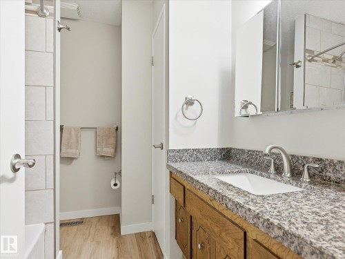 Bathroom featuring a single vanity with stone countertop, undermount sink, and wood-finish cabinetry - 18627 62A Avenue, Edmonton, AB - Indoor Photo Showing Bathroom
