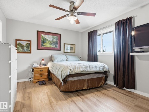 Bedroom featuring wood-finish flooring, a ceiling fan with integrated lighting, a window with dark drapery, and neutral wall paint - 18627 62A Avenue, Edmonton, AB - Indoor Photo Showing Bedroom