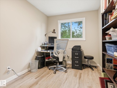 Room featuring wood-finish flooring, a window with exterior tree views, a neutral wall color, and built-in shelving - 18627 62A Avenue, Edmonton, AB - Indoor Photo Showing Office