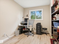Room featuring wood-finish flooring, a window with exterior tree views, a neutral wall color, and built-in shelving - 