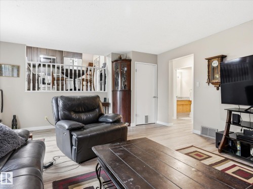 Living space featuring light wood-finish flooring, a white spindle railing separating the upper kitchen area, and a doorway leading to a room with a wood vanity and light countertop - 18627 62A Avenue, Edmonton, AB - Indoor Photo Showing Living Room