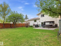Expansive backyard featuring a manicured lawn, established trees, and a wooden privacy fence - 