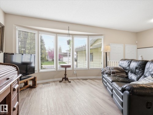 Spacious living area featuring a large bay window with horizontal blinds, light wood-finish flooring, and neutral wall paint - 18627 62A Avenue, Edmonton, AB - Indoor Photo Showing Living Room