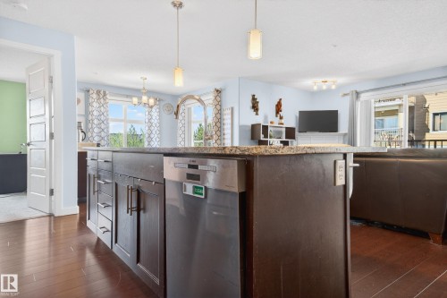 Kitchen island featuring dark wood cabinetry, stainless steel dishwasher, and a stone countertop - 340 6076 Schonsee Way, Edmonton, AB - Indoor Photo Showing Kitchen With Upgraded Kitchen