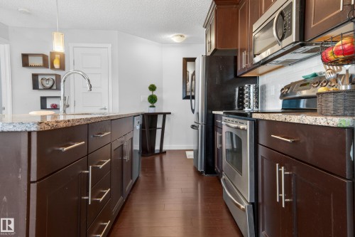 Kitchen with dark wood-finish cabinetry, granite countertops, and stainless steel appliances - 340 6076 Schonsee Way, Edmonton, AB - Indoor Photo Showing Kitchen With Stainless Steel Kitchen With Upgraded Kitchen