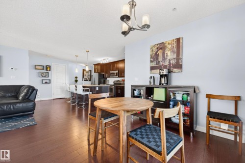 Open-concept living space featuring wood-finish flooring, a kitchen island with pendant lighting, and a defined dining area - 340 6076 Schonsee Way, Edmonton, AB - Indoor