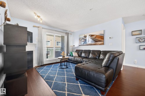 Living area featuring rich wood-finish flooring and a light blue wall color - 340 6076 Schonsee Way, Edmonton, AB - Indoor Photo Showing Living Room With Fireplace