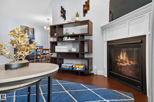 Living area featuring a corner-mounted fireplace with white paneled surround, dark wood-finish flooring, and light wall tones - 340 6076 Schonsee Way, Edmonton, AB - Indoor With Fireplace