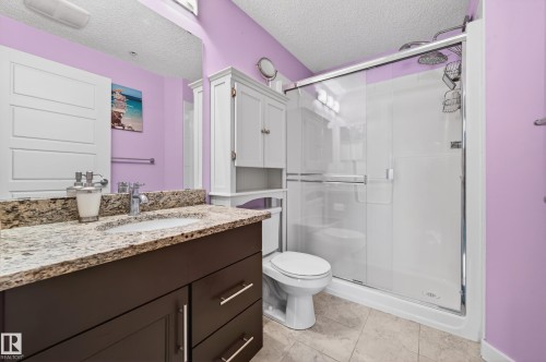 Spacious bathroom featuring a dark wood-finish vanity with a granite-style countertop and integrated sink - 340 6076 Schonsee Way, Edmonton, AB - Indoor Photo Showing Bathroom
