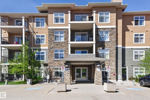 Multi-story building facade featuring stone accents, horizontal siding, multiple balconies with black railings, a covered entryway, and mature trees - 340 6076 Schonsee Way, Edmonton, AB - Outdoor With Balcony With Facade