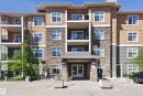 Multi-story building facade featuring stone accents, horizontal siding, multiple balconies with black railings, a covered entryway, and mature trees - 340 6076 Schonsee Way, Edmonton, AB  - Outdoor With Balcony With Facade 