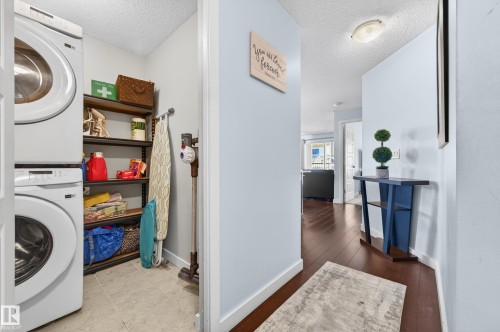 Dedicated laundry area featuring stacked appliances and shelving - 340 6076 Schonsee Way, Edmonton, AB - Indoor Photo Showing Laundry Room