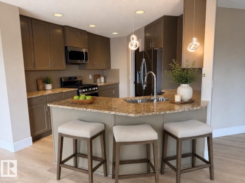 Modern kitchen featuring a breakfast bar with seating, granite countertops, stainless steel appliances, recessed lighting, and wood-finish flooring - 648 178 Street, Edmonton, AB - Indoor Photo Showing Kitchen With Double Sink With Upgraded Kitchen