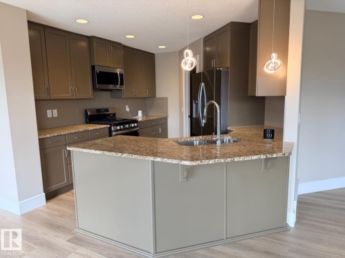 Kitchen featuring an angular island with an undermount double basin sink, granite countertops, and light wood-finish flooring - 648 178 Street, Edmonton, AB - Indoor Photo Showing Kitchen With Double Sink With Upgraded Kitchen