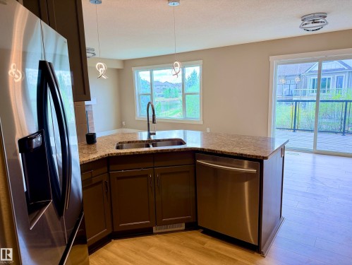 Kitchen area featuring dark wood-finish cabinetry, a curved peninsula with a speckled countertop, a stainless steel undermount double-basin sink, and a stainless steel dishwasher - 648 178 Street, Edmonton, AB - Indoor Photo Showing Kitchen With Double Sink