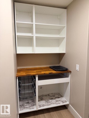 Built-in desk area featuring white cabinetry, a wood-finish countertop, adjustable shelving, and integrated wire pull-out baskets - 648 178 Street, Edmonton, AB - Indoor With Storage