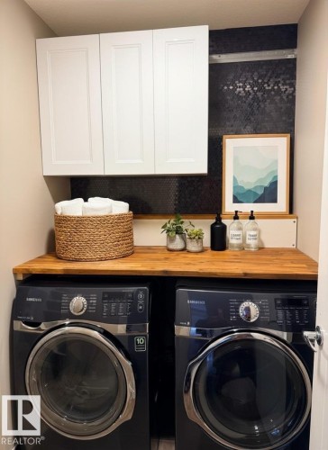 Dedicated laundry space featuring a wood-finish countertop, dark hexagonal tile backsplash, and white upper cabinetry - 648 178 Street, Edmonton, AB - Indoor Photo Showing Laundry Room
