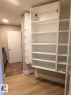 Built-in shelving and cabinetry with glass-fronted sections, wood-finish flooring, white baseboards, and neutral wall tones - 
