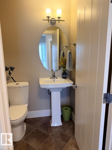 Pedestal sink with an oval mirror and two-light vanity fixture - 648 178 Street, Edmonton, AB - Indoor Photo Showing Bathroom