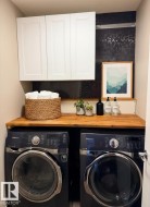 Laundry area featuring a wood-finish countertop, white upper cabinetry, and dark hexagon tile backsplash - 