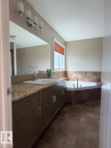 Bathroom with a corner soaking tub and a vanity featuring an integrated sink, granite-finish countertop, and dark wood cabinetry - 648 178 Street, Edmonton, AB - Indoor Photo Showing Bathroom