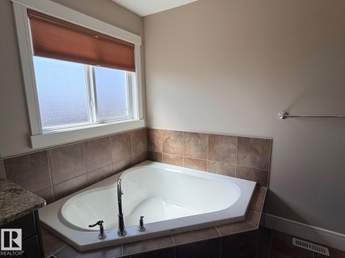 Corner soaking tub featuring a deck-mounted faucet, tile surround, and a frosted window with a pleated blind - 648 178 Street, Edmonton, AB - Indoor Photo Showing Bathroom