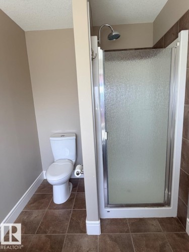 Bathroom featuring a walk-in shower with a frosted glass door, a classic white toilet, and square brown floor tiling - 648 178 Street, Edmonton, AB - Indoor Photo Showing Bathroom