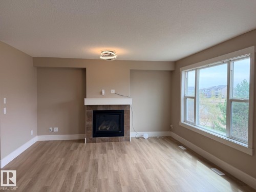Living area featuring wood-finish flooring and a tiled fireplace with a white mantel - 648 178 Street, Edmonton, AB - Indoor Photo Showing Living Room With Fireplace