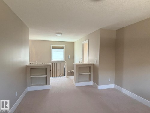 Carpeted loft area featuring built-in shelving, neutral wall tones, white trim, and a window with blinds - 648 178 Street, Edmonton, AB - Indoor Photo Showing Other Room