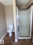 Bathroom featuring a glass-enclosed shower with a rain showerhead, a white toilet, and brown tile flooring - 