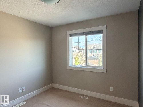 Bright interior space featuring a window with white trim, beige wall paint, white baseboards, and carpeted flooring - 648 178 Street, Edmonton, AB - Indoor Photo Showing Other Room