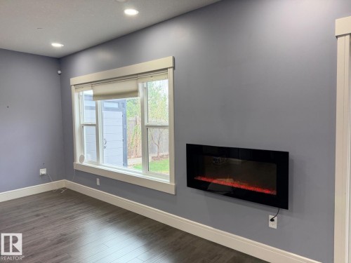 Spacious interior featuring a wall-mounted electric fireplace, recessed ceiling lighting, light blue walls, dark wood-finish flooring, and white trim - 648 178 Street, Edmonton, AB - Indoor With Fireplace
