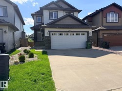 Contemporary two-story residence featuring a two-car garage with white panel doors, stone façade accents, and a concrete driveway - 