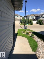 Concrete walkway leading to a landscaped front yard with green lawn, decorative shrubs, and pebble accents - 