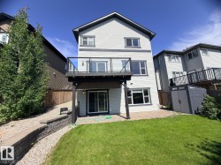 Two-story rear exterior featuring a ground-level patio with paver stones, a second-story deck with glass railing, a sliding glass door, multiple windows, and a storage shed - 