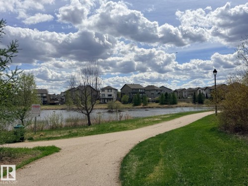 Paved walking path bordered by manicured grass and mature shrubs - 648 178 Street, Edmonton, AB - Outdoor With View