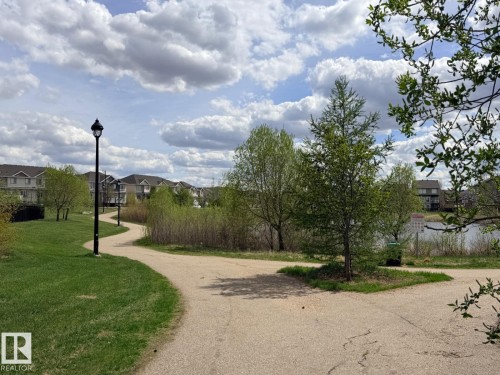 Paved walking path alongside a grassy area with mature trees and a body of water - 648 178 Street, Edmonton, AB - Outdoor With View