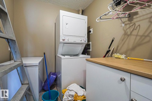 Dedicated laundry area featuring a stacked washer and dryer, white base cabinetry with a wood-finish countertop, and wall-mounted shelving - 314 5340 199 Street, Edmonton, AB - Indoor Photo Showing Laundry Room