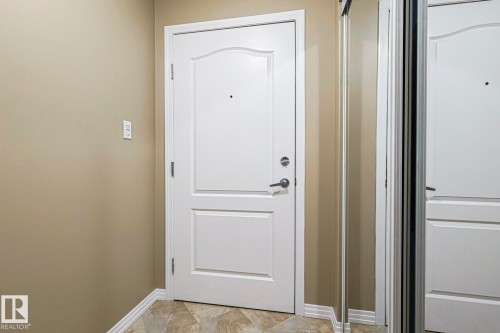 Entryway featuring a white paneled door with brushed nickel hardware, neutral wall paint, tile flooring, and mirrored closet doors - 314 5340 199 Street, Edmonton, AB - Indoor Photo Showing Other Room