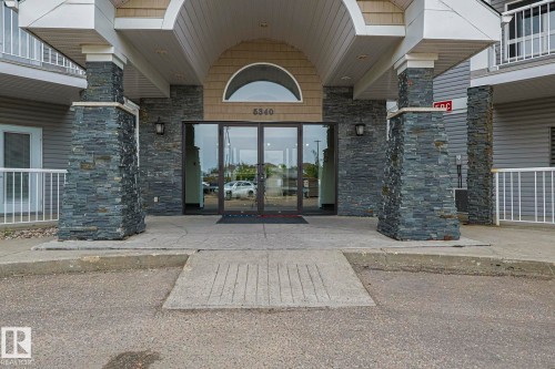 Building entrance featuring stacked stone pillars, large glass double doors, an arched transom window, and a covered entry - 314 5340 199 Street, Edmonton, AB - Outdoor