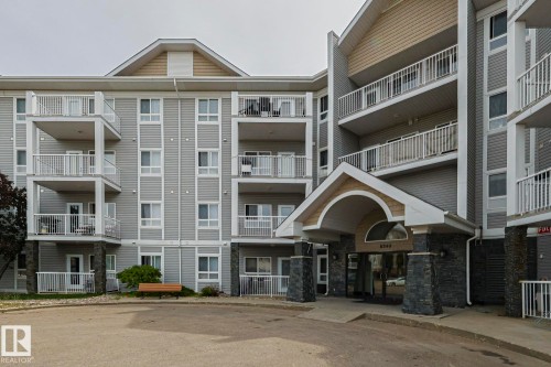 Multi-story building featuring gray horizontal siding, multiple balconies with white railings, and a prominent covered entryway - 314 5340 199 Street, Edmonton, AB - Outdoor With Facade