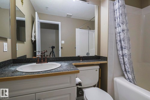 Bathroom featuring a white vanity with paneling, dark speckled countertop, and an undermount sink with a bronze-finish faucet - 314 5340 199 Street, Edmonton, AB - Indoor Photo Showing Bathroom