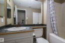 Bathroom featuring a white vanity with paneling, dark speckled countertop, and an undermount sink with a bronze-finish faucet - 314 5340 199 Street, Edmonton, AB  - Indoor Photo Showing Bathroom 