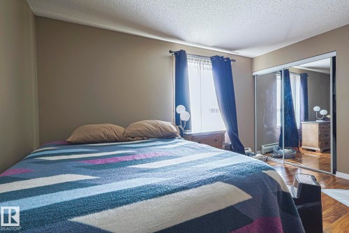 Interior room featuring smooth painted walls, wood-finish flooring, a window with curtains, and mirrored sliding closet doors - 314 5340 199 Street, Edmonton, AB - Indoor Photo Showing Bedroom